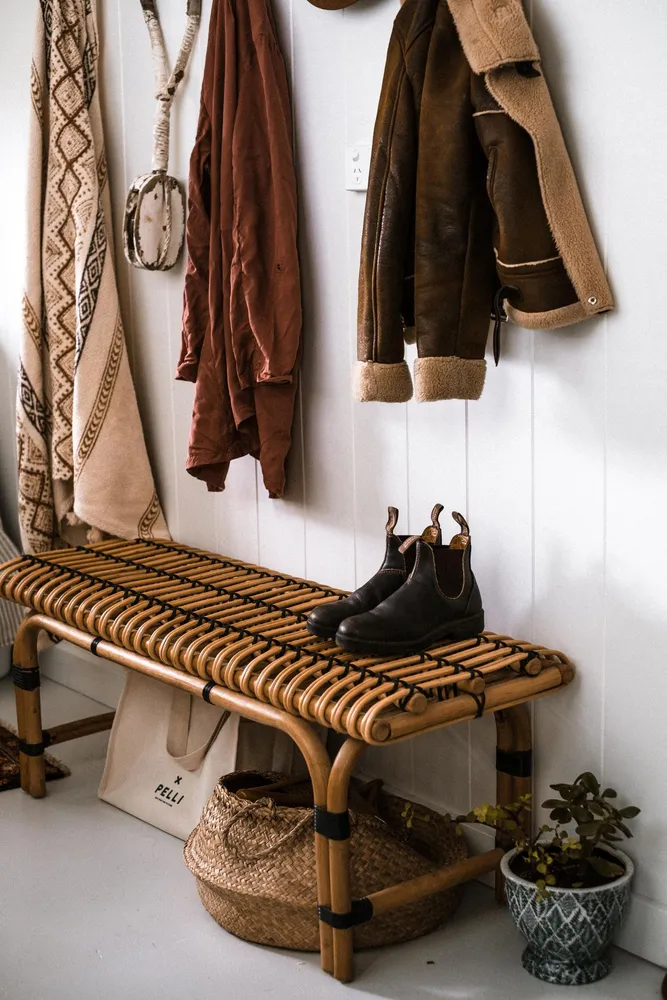 Coats and shoes arranged around a woven entryway bench